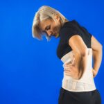 woman-pain-from-back-injury-wearing-lumbar-brace-corset-blue-background-copy-space_wp