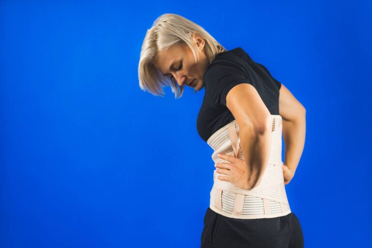 woman-pain-from-back-injury-wearing-lumbar-brace-corset-blue-background-copy-space_wp